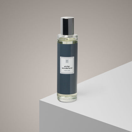 A Winter Wonderland Mist glass spray bottle with black cap sits on a white geometric surface against a neutral background, adding a fresh, seasonal scent to your space.