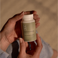 A person holds a bottle labeled Multipack - Natural Ashwagandha (4 Month Supply), known for immune support and often called Indian ginseng. Soft lighting and light blue clothing create a calm atmosphere.