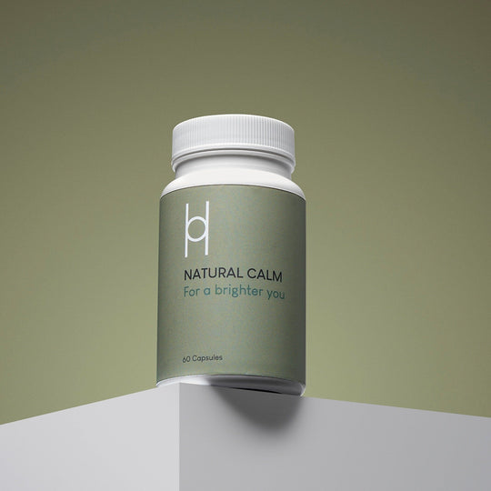 A grayish-green bottle labeled "Natural Calm Supplement - 5-HTP Stress Relief, Anxiety & Mood Support - 60 Capsules" with a white cap sits on a white surface against a greenish background.