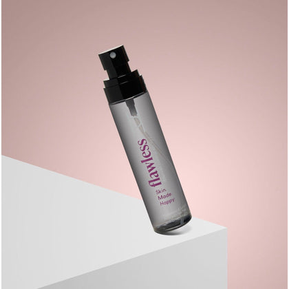 A clear spray bottle of Flawless Blemish Control Spray (Hyaluronic & Salicylic Acid, 100ml) with a black cap, displayed at an angle on a white geometric surface against a soft pink gradient background.