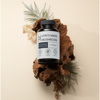 A bottle of Lion's Mane Mushroom Supplement 800mg Per Serving (60 capsules, 30-day supply) is shown on driftwood with green foliage and a beige background. The label features minimalist icons for brain function and cognitive health benefits.