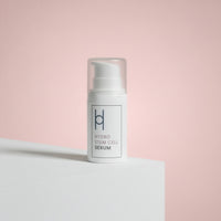 A white bottle from the Women's Skin Reset Gift Set | 4-Piece Anti-Ageing Collection, featuring Hydro Stem Cell Serum with a pump, rests on a white surface with a pink background, its label highlighting synergy for radiant, revitalized skin.