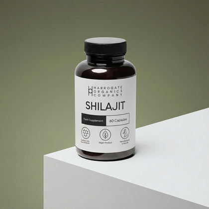 A dark bottle labeled Shilajit Supplement 1000mg Per Serving - 30 Day Supply - 60 Capsules sits on a white platform, highlighting its vegan, non-GMO, heavy metal-tested ayurvedic formula.