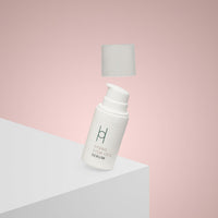A white bottle from the Ultimate Women's Skincare Set | Complete 6-Piece Collection rests on a white surface with a pink background, its cap floating above—perfectly capturing your journey to radiant skin.