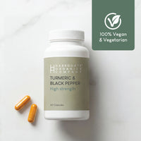 A bottle of Turmeric & Black Pepper Supplement - High Strength (2500mg per serving, 60 capsules, 30 day supply) from Harrogate Organics Company sits on a white surface with two capsules. A green icon displays "100% Vegan & Vegetarian" with a leaf symbol.