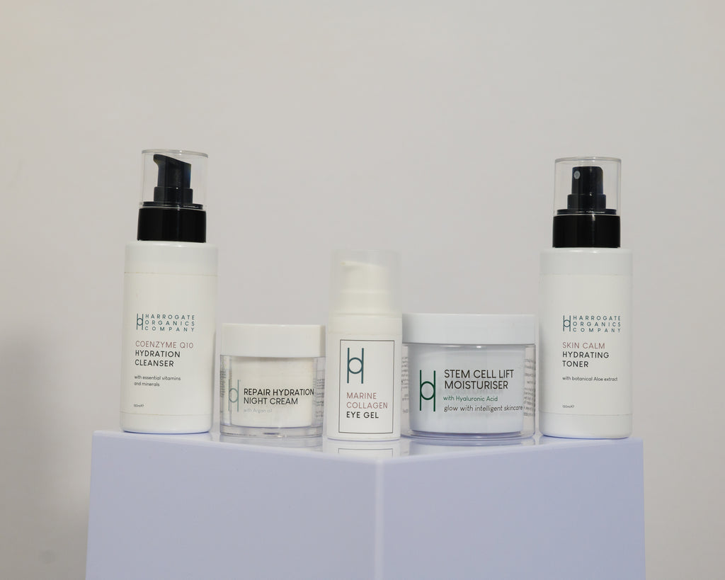 The Ultimate Men's Skincare Routine from Harrogate Organics Company features five white containers—cleanser, night cream, eye gel, moisturizer, and toner—arranged on a white pedestal to support healthy skin for all.