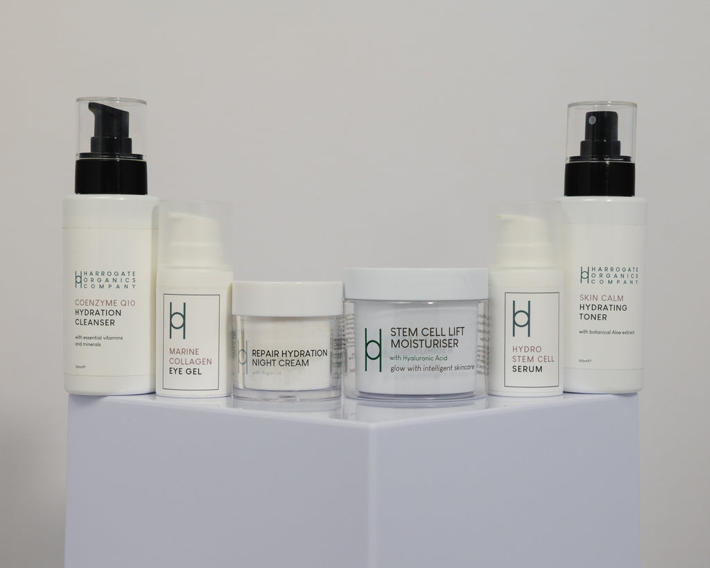 The Ultimate Women's Skincare Routine, featuring cleansers, creams, serums, and toners with white labels and green and black text, is displayed neatly on a white pedestal—ideal for radiant skin.