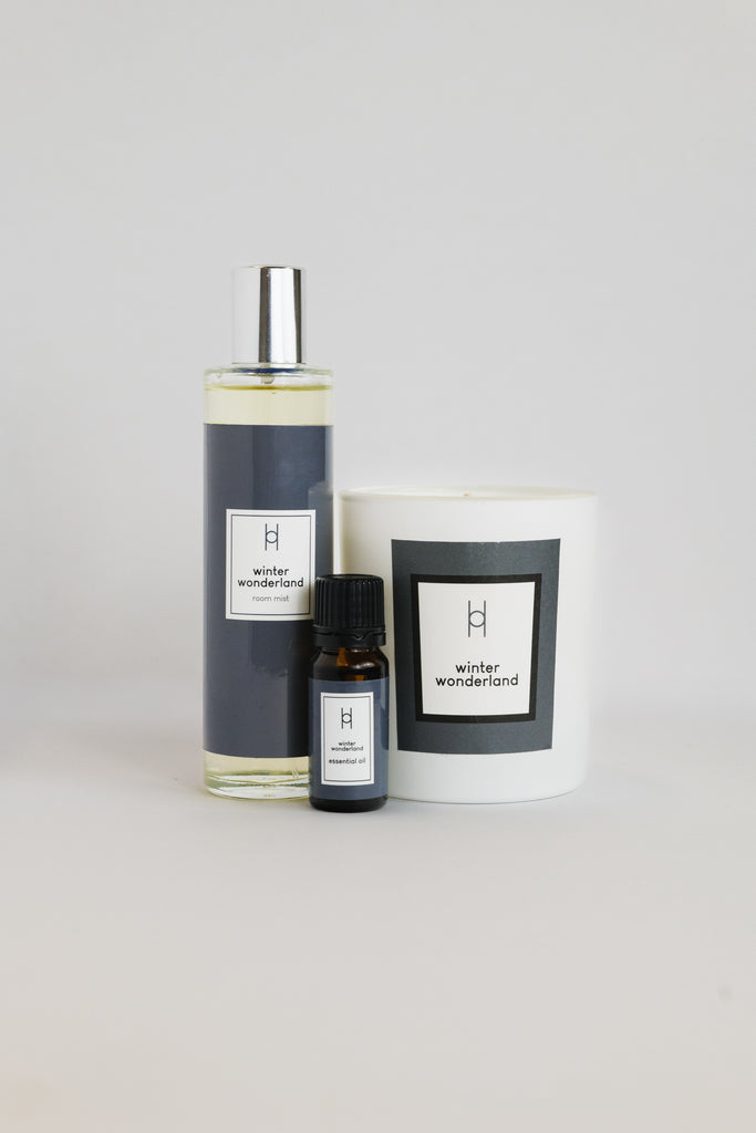 The Deluxe Home Collection - Winter Wonderland features a clear spray bottle, a small dark essential oil dropper, and a hand-poured candle, all labeled with the fragrance and arranged against a plain light background.