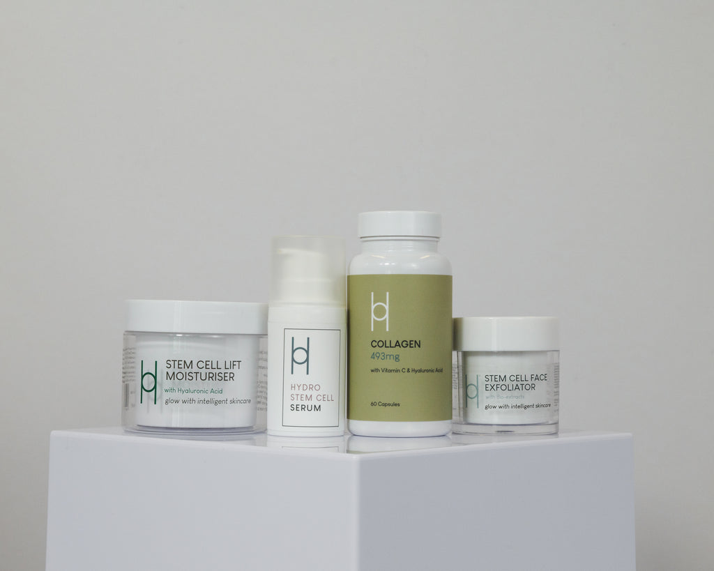 Women's Skin Reset is displayed on a white platform in minimalist white and green packaging, featuring a moisturizer, hydro stem cell serum, collagen supplement capsules, and a face exfoliator.