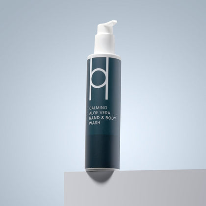 A 250ml bottle of Aloe Vera Hand & Body Wash | Gentle Natural Cleanser, labelled in white text on a dark green background with a pump dispenser, sits on a light gray surface against a pale blue backdrop.