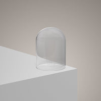 The Hand-Blown Luxury Glass Candle Cloche - Recycled sits on a white platform against a beige background, its sleek glass reflecting light—an elegant, eco-friendly accessory for gifting or displaying candles.