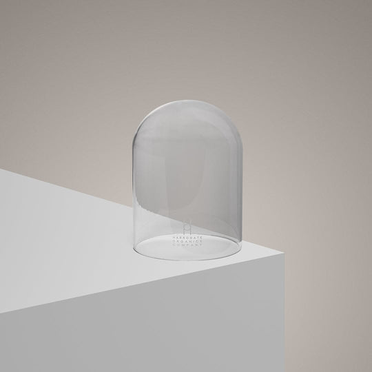 The Hand-Blown Luxury Glass Candle Cloche - Recycled sits on a white platform against a beige background, its sleek glass reflecting light—an elegant, eco-friendly accessory for gifting or displaying candles.