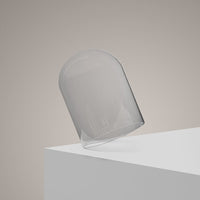 The Hand-Blown Luxury Glass Candle Cloche - Recycled is artfully tilted on a white rectangular surface, set against a soft beige backdrop. The well-lit scene highlights the cloche’s elegant, minimalist design.