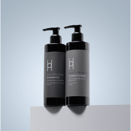 Two black pump bottles of Natural Shampoo & Conditioner Duo - Natural Greatness for Normal Hair stand side by side on a white surface against a light blue-gray background.