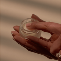 A manicured hand dips into a jar of Lip Conditioning Balm with Peppermint, its creamy texture ready to soothe chapped lips. The soft, warm lighting highlights the natural formula, perfect for nourishing lips anytime.