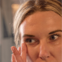 A person gently applies Marine Collagen Eye Gel with hyaluronic acid, avocado oil, and green tea extract under their right eye to target dark circles. The close-up image highlights the face and hand.