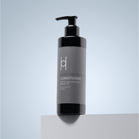 A black pump bottle of Moisture Protect Conditioner – With Pomegranate Seed and Baobab Oils, 250ml, sulfate-free, sits on a white surface with a light blue gradient background.