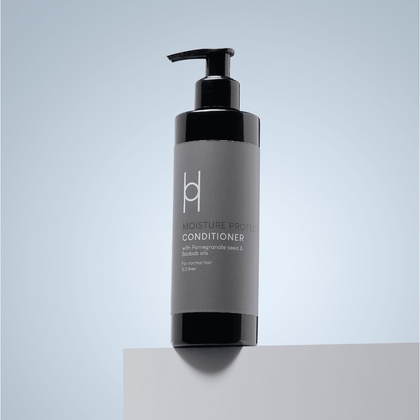 A black pump bottle of Moisture Protect Conditioner – With Pomegranate Seed and Baobab Oils, 250ml, sulfate-free, sits on a white surface with a light blue gradient background.