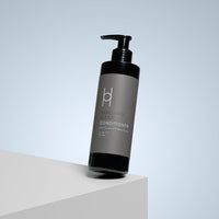 A black bottle of Enriching Repair Conditioner with Coconut & Marula Oils (250ml) and a dispenser sits on a white surface; it's sulphate free for revitalising hair care.
